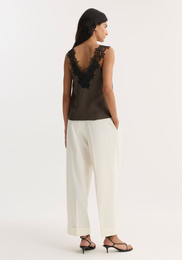 Woman models V-neck silk lace top | earth, showing back lace inset, paired with high-waisted, wide-leg trousers and low-heeled sandals, emphasizing elegant design.