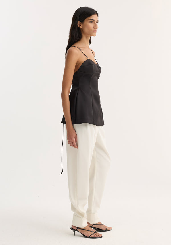 Profile view of a person wearing a Bustier top | black with spaghetti straps, bustier stitching, and a fitted waist, paired with white high-waisted trousers.
