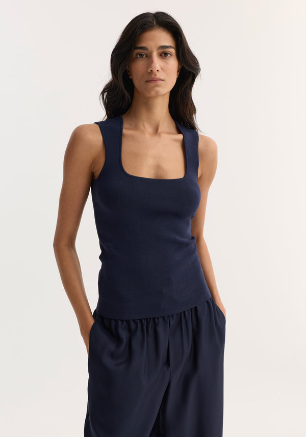 Model wearing Bustier shaped knitted top | navy, featuring a sleeveless design and bustier neckline, paired with loose-fitting trousers, hands in pockets.