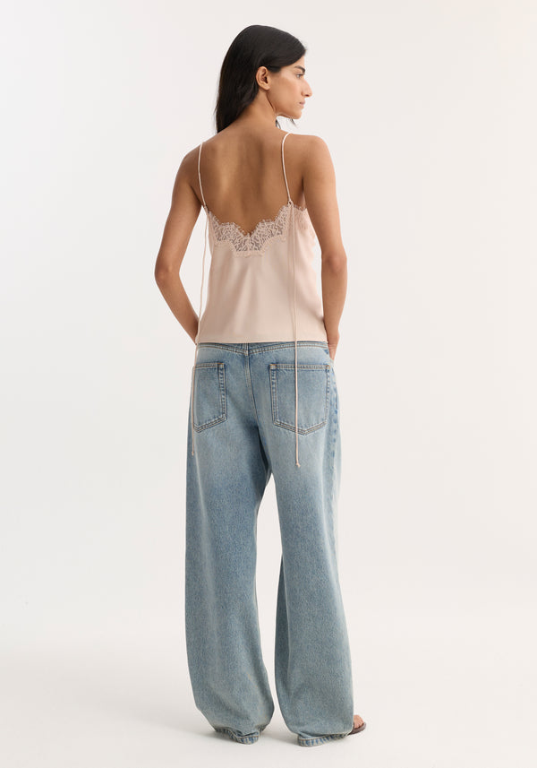 Woman wearing Lace silk camisole | rose with lace trim and spaghetti straps, paired with loose-fit jeans. Hair is dark and straight, falling past shoulders.