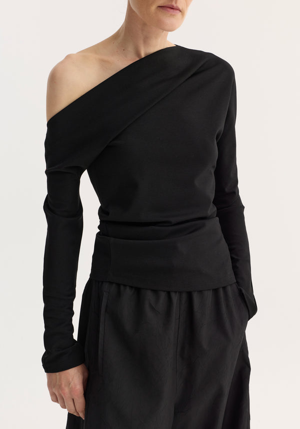 Model wearing a black Twisted jersey top with one-shoulder design and long sleeves, paired with a skirt featuring side pockets, highlighting a sculpted waist.