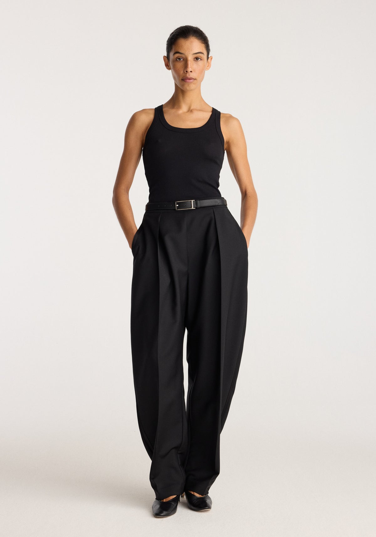 Merino scoop neck top | black worn by a model with black tailored trousers and hands in pockets against a neutral studio background