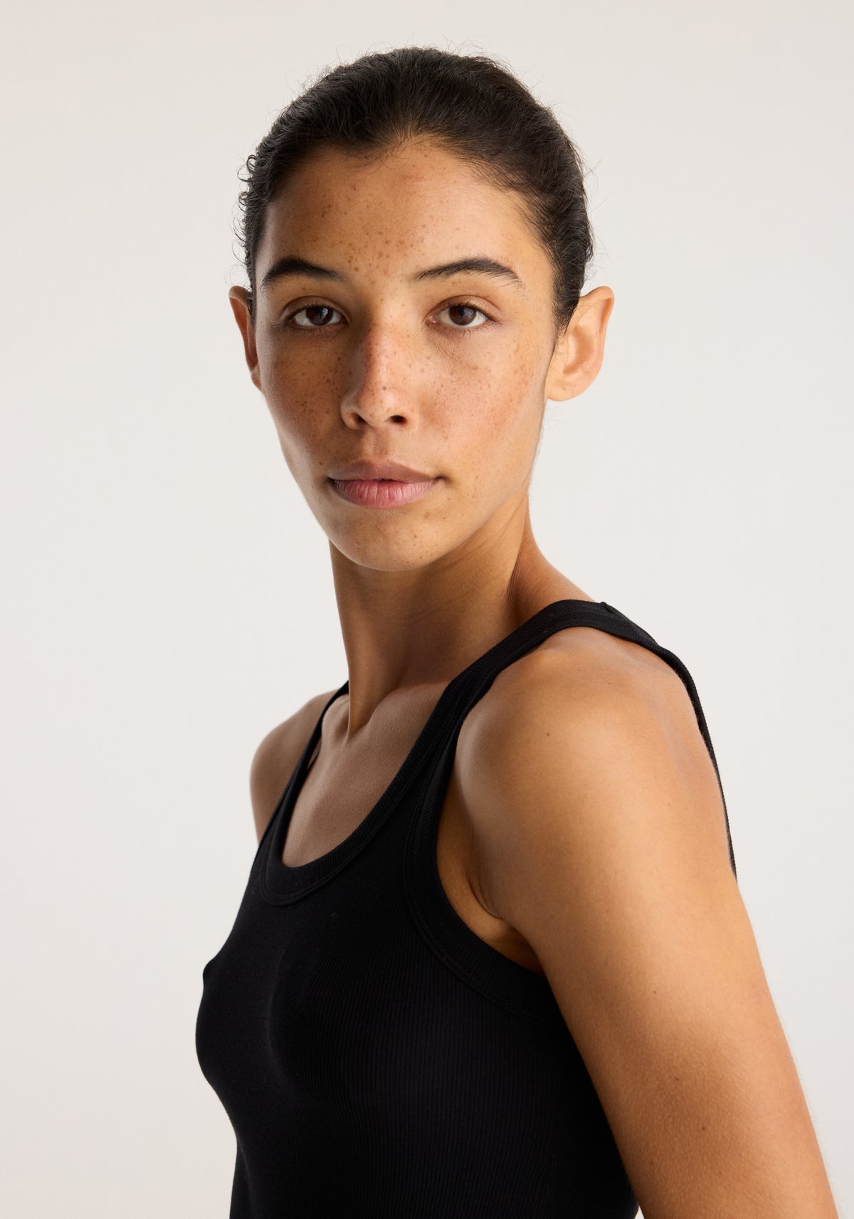 Merino scoop neck top | black worn by a model in a studio portrait showing its close fitting scoop neckline and sleeveless design