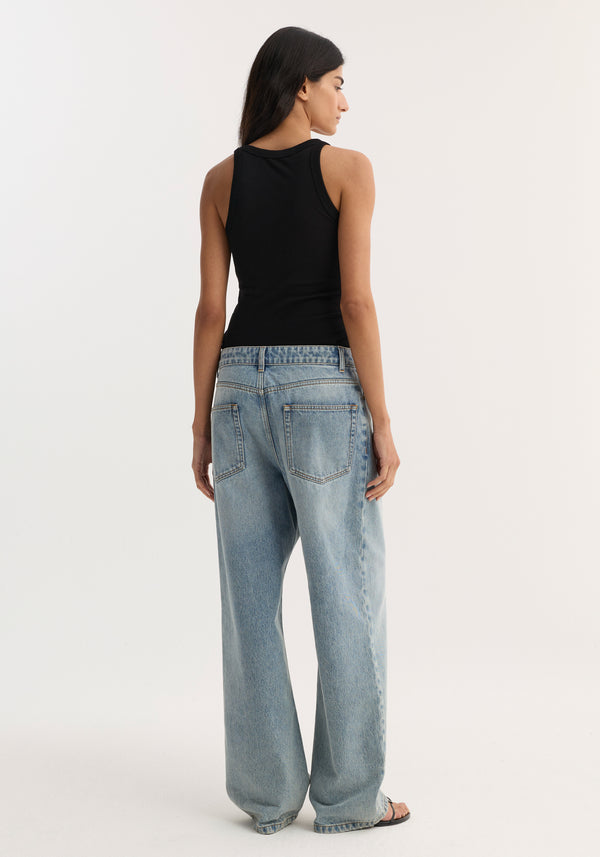 Merino scoop neck top in black, worn by a young woman, showcasing its sleeveless, fitted design paired with loose-fit jeans and sandals.