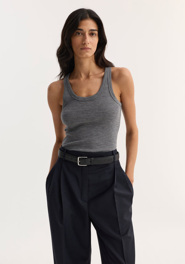Model wearing Merino scoop neck top in mid grey melange, tucked into high-waisted trousers, showcasing its sleeveless, fitted design crafted from 100% merino wool.