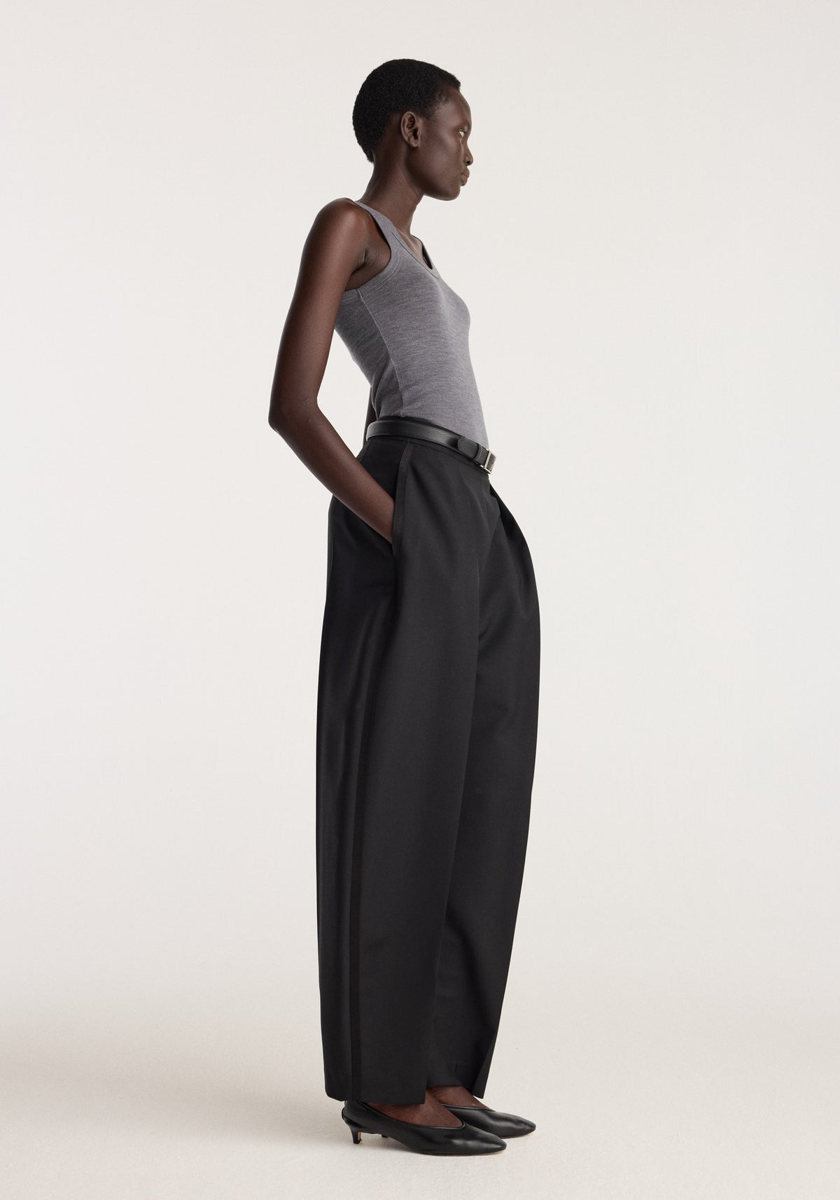 Merino scoop neck top | mid grey melange worn by a model with black wide leg trousers in a side profile studio image