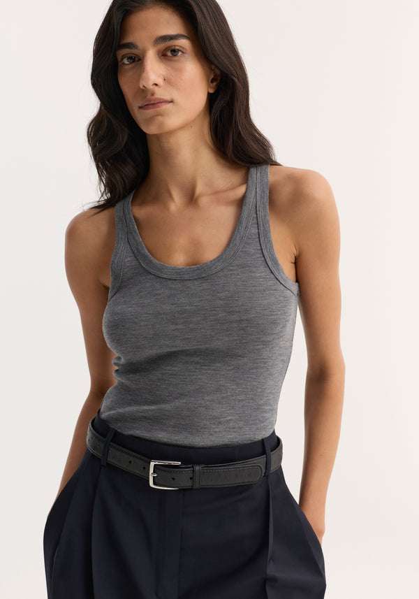 Model wearing a Merino scoop neck top in mid grey melange, tucked into high-waisted navy trousers, accessorized with a black belt.