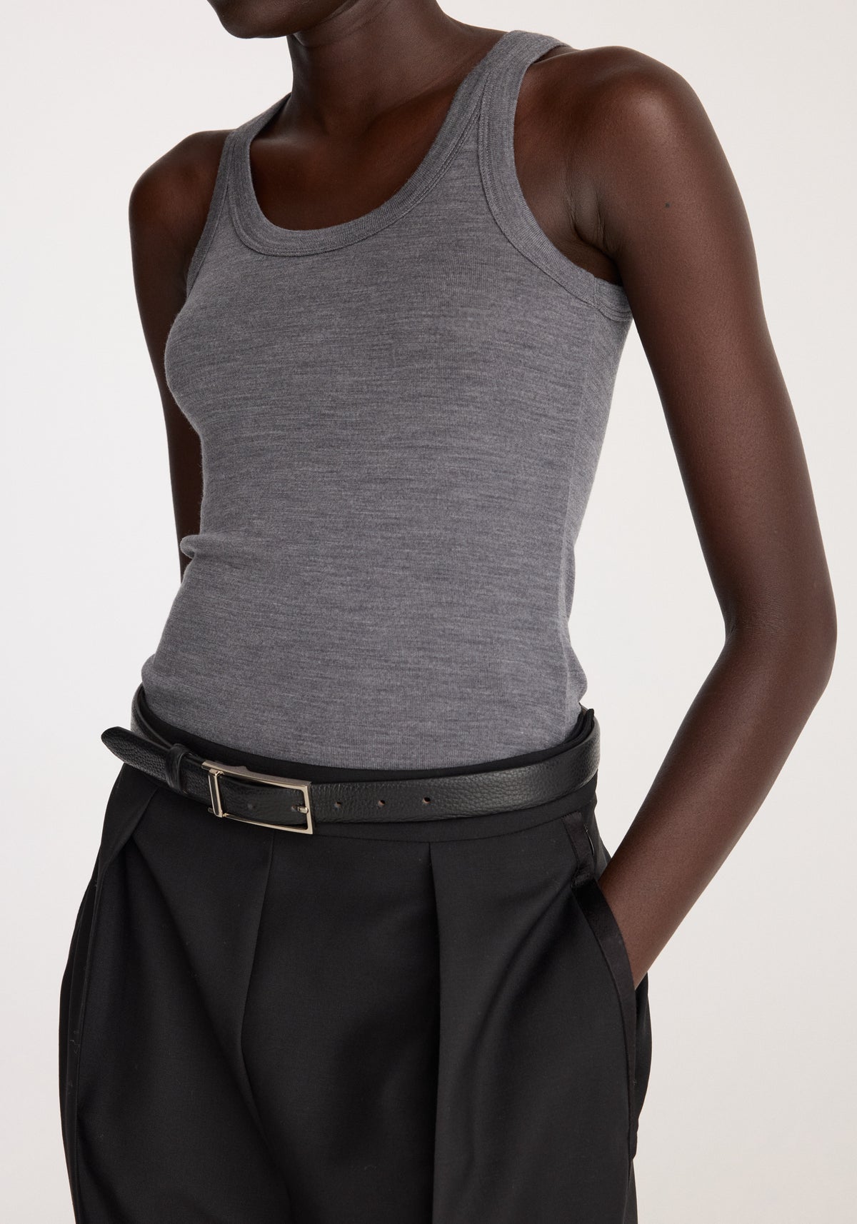 Merino scoop neck top | mid grey melange worn with black pleated trousers on a model posing with one hand in a pocket