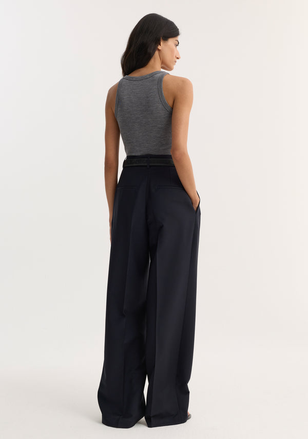 Merino scoop neck top in mid grey melange, worn tucked into high-waisted wide-leg trousers with a belt; model's back slightly turned, showcasing the sleeveless design.