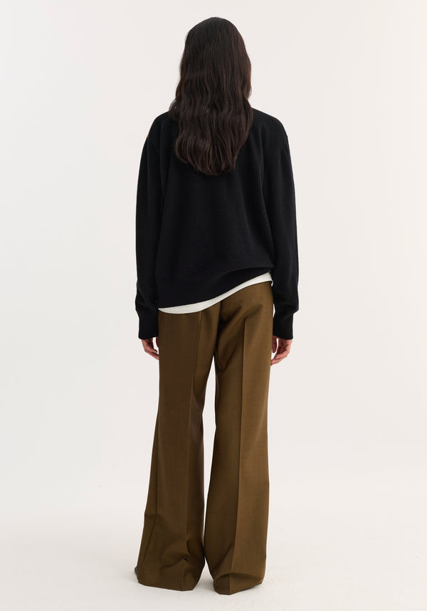 Person wearing a black rust check compact knitted polo with a structured collar and three-button front, layered over a white top and paired with brown trousers.