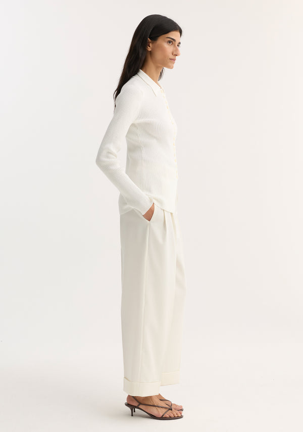 Woman in profile wearing an Elongated rib cardigan, off white, with button closures and collar, paired with high-waisted, wide-leg trousers and strappy sandals.