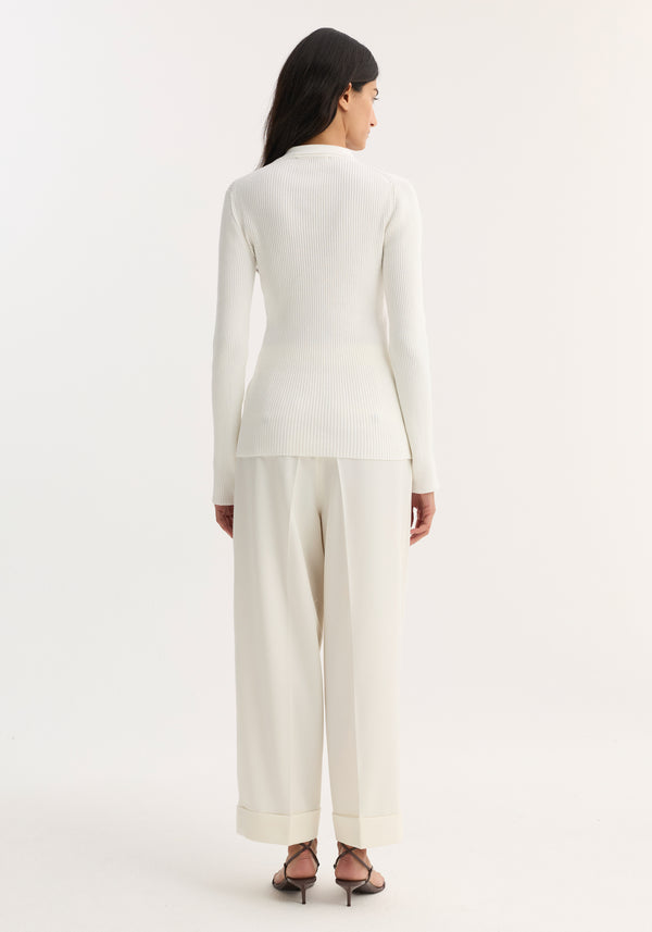 Woman in off-white elongated rib cardigan with collar and buttons, paired with wide-leg trousers and strappy sandals, showcasing a sleek, sophisticated look.