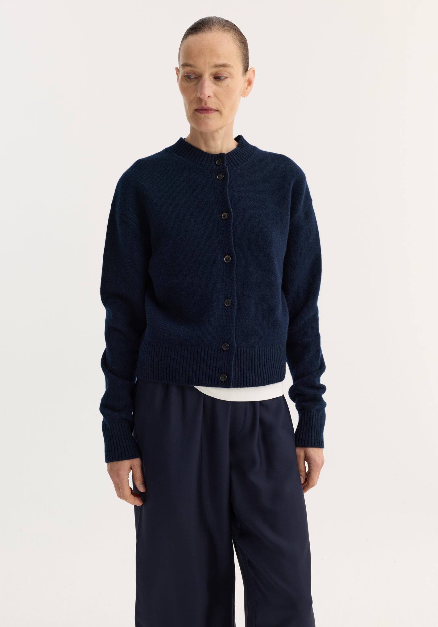 Woman wearing a Short boiled cardigan | navy, featuring a high crew neck, drop shoulders, ribbed cuffs, and hem, paired with wide-leg trousers.