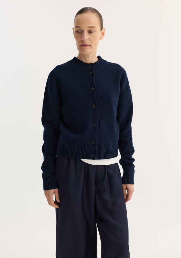 Woman wearing a Short boiled cardigan | navy, featuring a high crew neck, drop shoulders, ribbed cuffs, and hem, paired with wide-leg trousers.