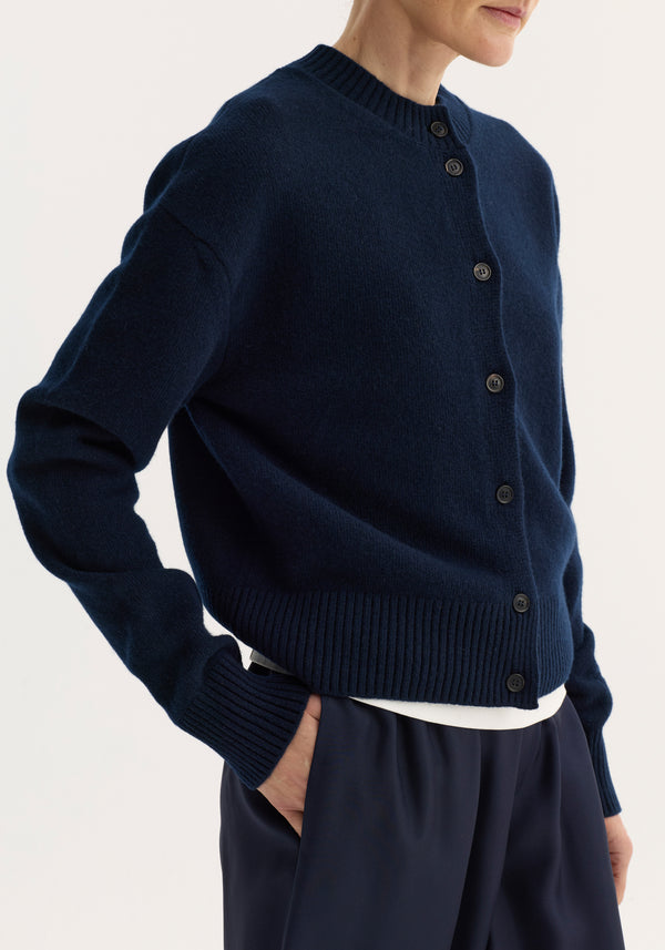 Model wearing the Short boiled cardigan in navy, featuring a ribbed crew neck, drop shoulders, dark buttons, and a soft, felted wool finish.