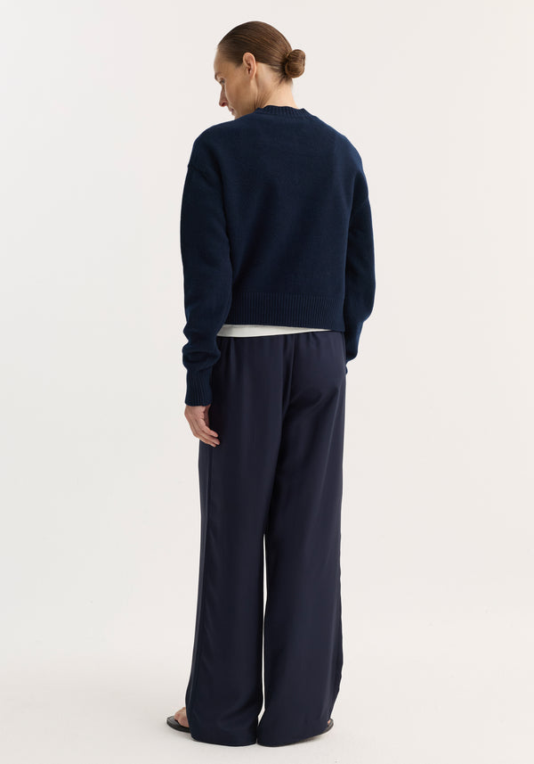 Person facing away, wearing a short boiled cardigan in navy with a high crew neck and drop shoulders, styled with matching wide-leg trousers.