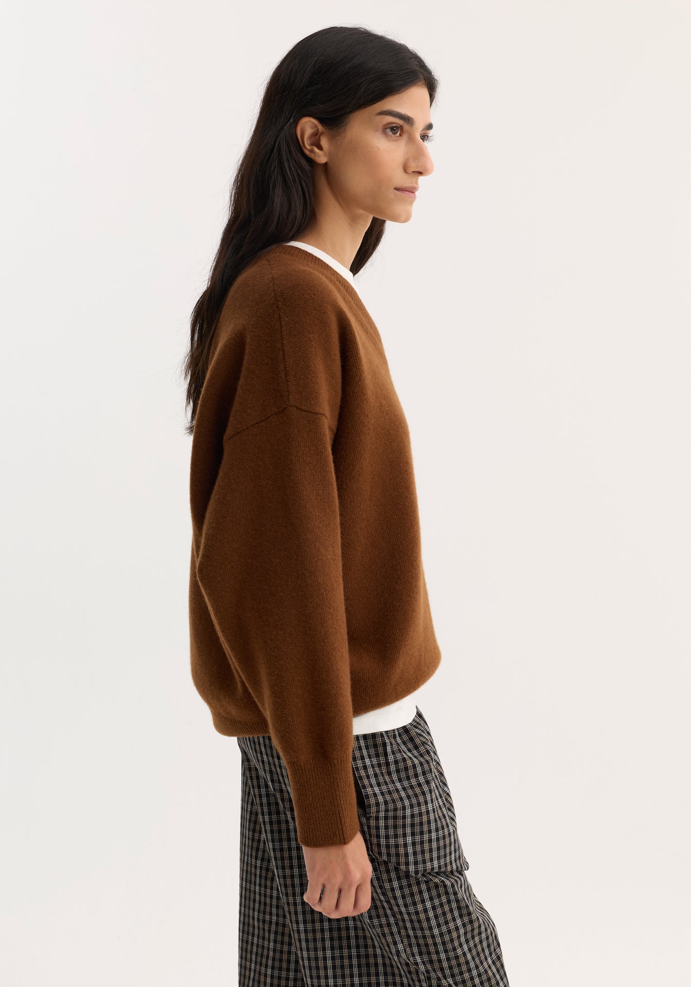 Woman in a rust V-neck knitted jumper with a relaxed fit and dropped shoulders, paired with checkered pants, showcasing an effortless, casual look.