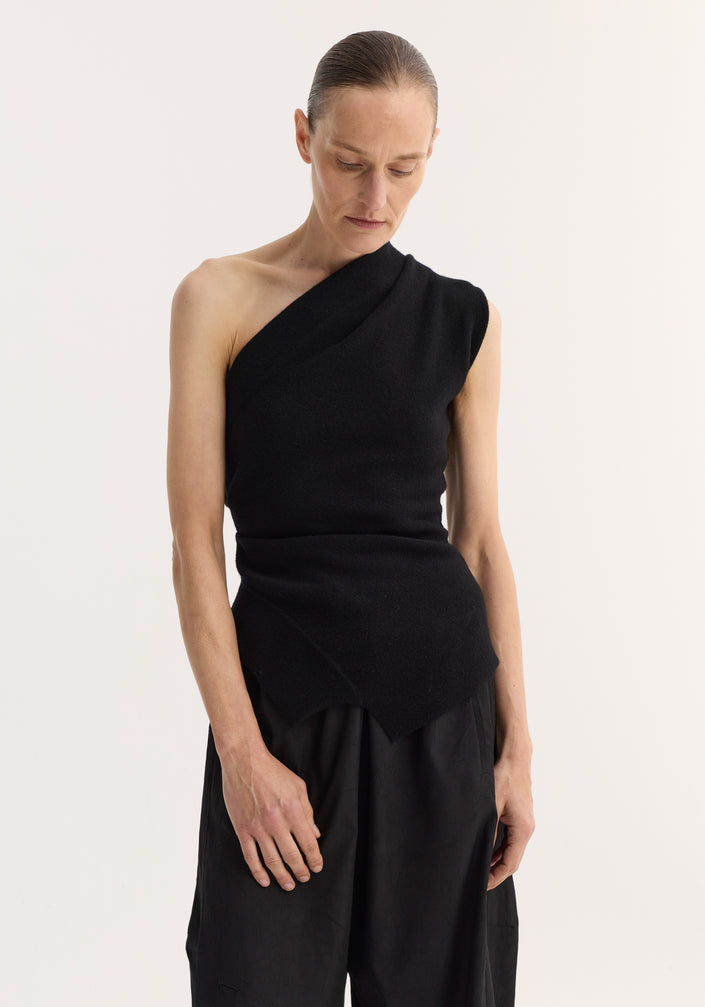 Off-shoulder top | black: Model wears a black, one-shoulder knit top with an asymmetrical hem and fitted waist, paired with harem-style trousers and open-toe sandals.