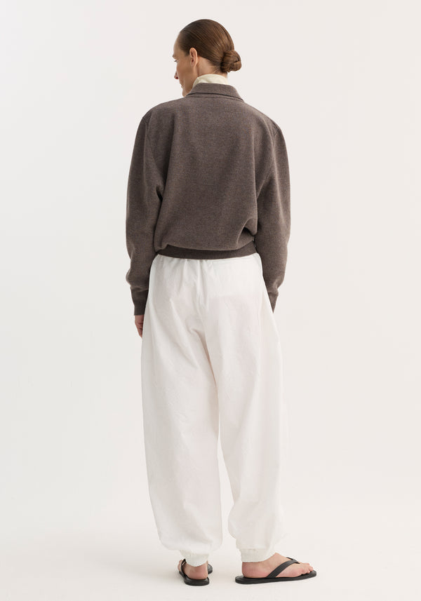 Person in Compact knitted polo with structured collar and three-button front, paired with voluminous white pants and black flip-flops, hair in low bun.