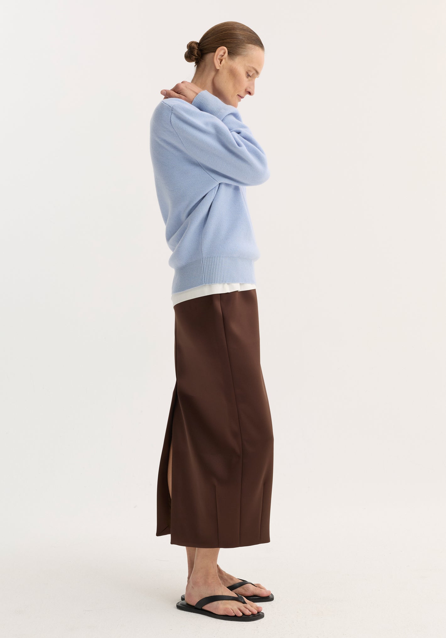 Side-profile of person wearing a baby blue compact knitted polo over a white top, paired with a brown skirt and black flip-flop sandals.