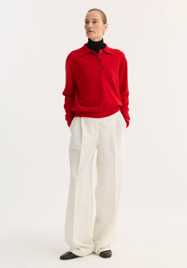 Model wearing a Wool Cashmere Polo | Red over a black turtleneck, paired with high-waisted white trousers, showcasing the polo's structured collar and three-button front.