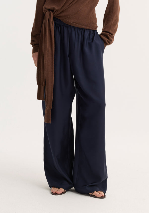 Wide leg silk trousers | night, featuring a relaxed drape and elasticated waistband with drawstring, worn with brown sandals and a tied long-sleeve top.