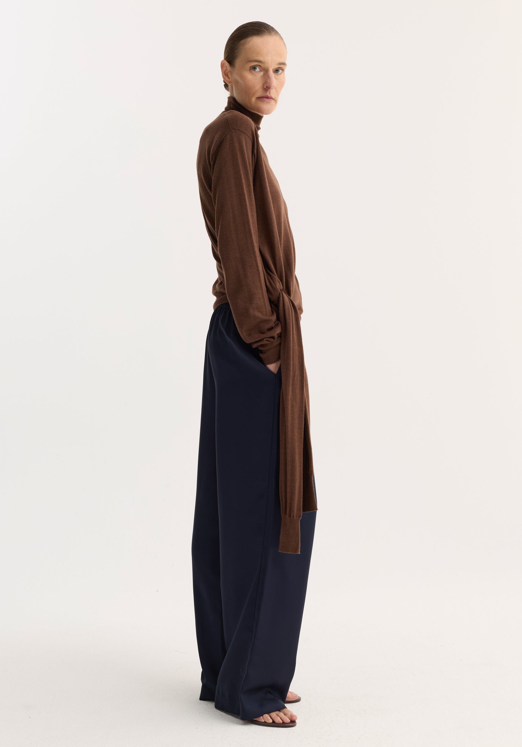 Woman in profile wearing Wide leg silk trousers | night, showcasing their relaxed drape and elasticated waistband with drawstring, paired with a knit top and sandals.