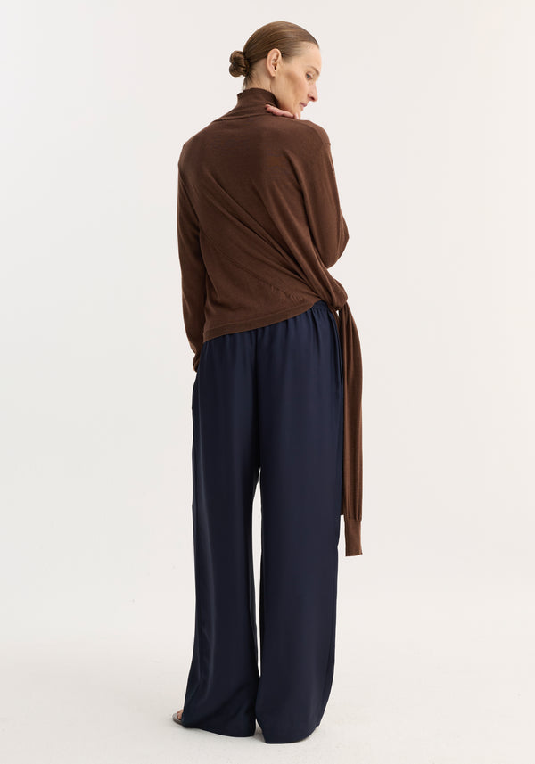 Woman wearing wide leg silk trousers with elasticated waistband and drawstring, styled with a brown turtleneck sweater, showcasing the trousers' relaxed drape and fluidity.