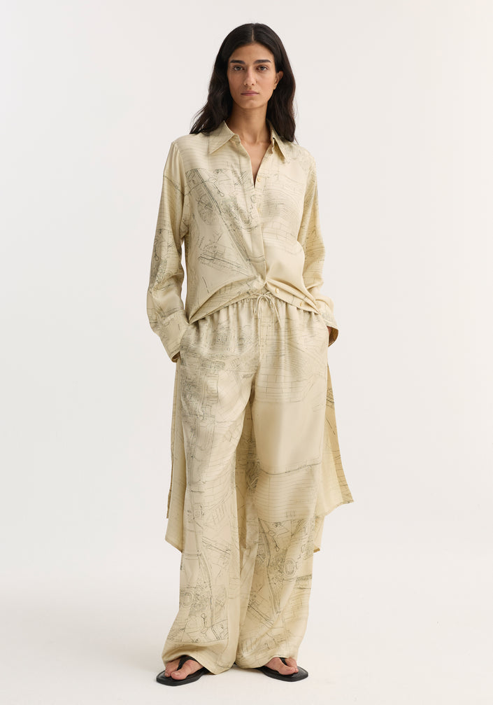 Woman in Wide leg silk trousers | Amsterdam, featuring archival map print, relaxed drape, elasticated waistband with drawstring, paired with matching button-down shirt and black sandals.