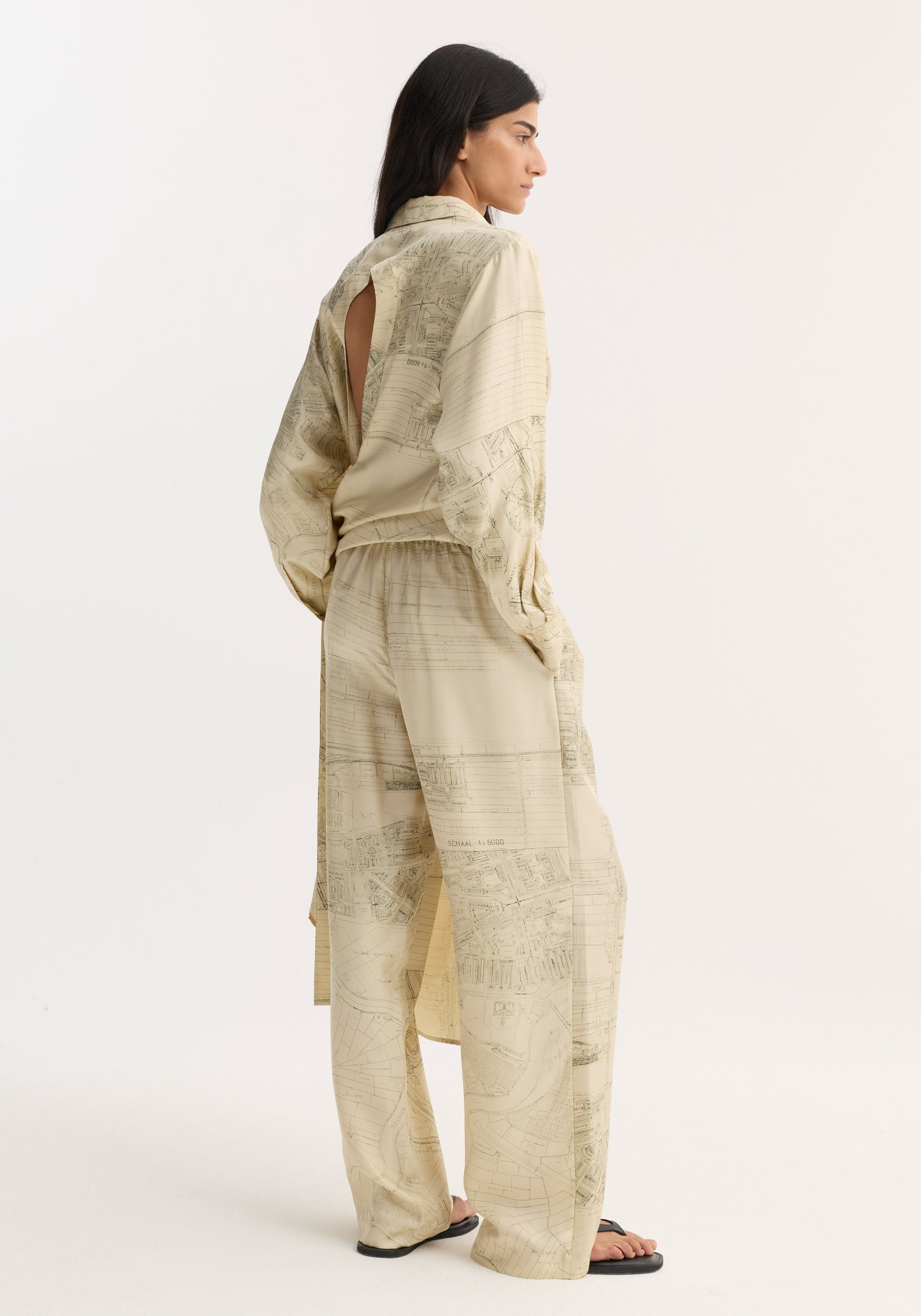 Model wearing Wide leg silk trousers | Amsterdam, featuring a relaxed drape, technical map print, elasticated waistband, and wide-leg silhouette, paired with black sandals.