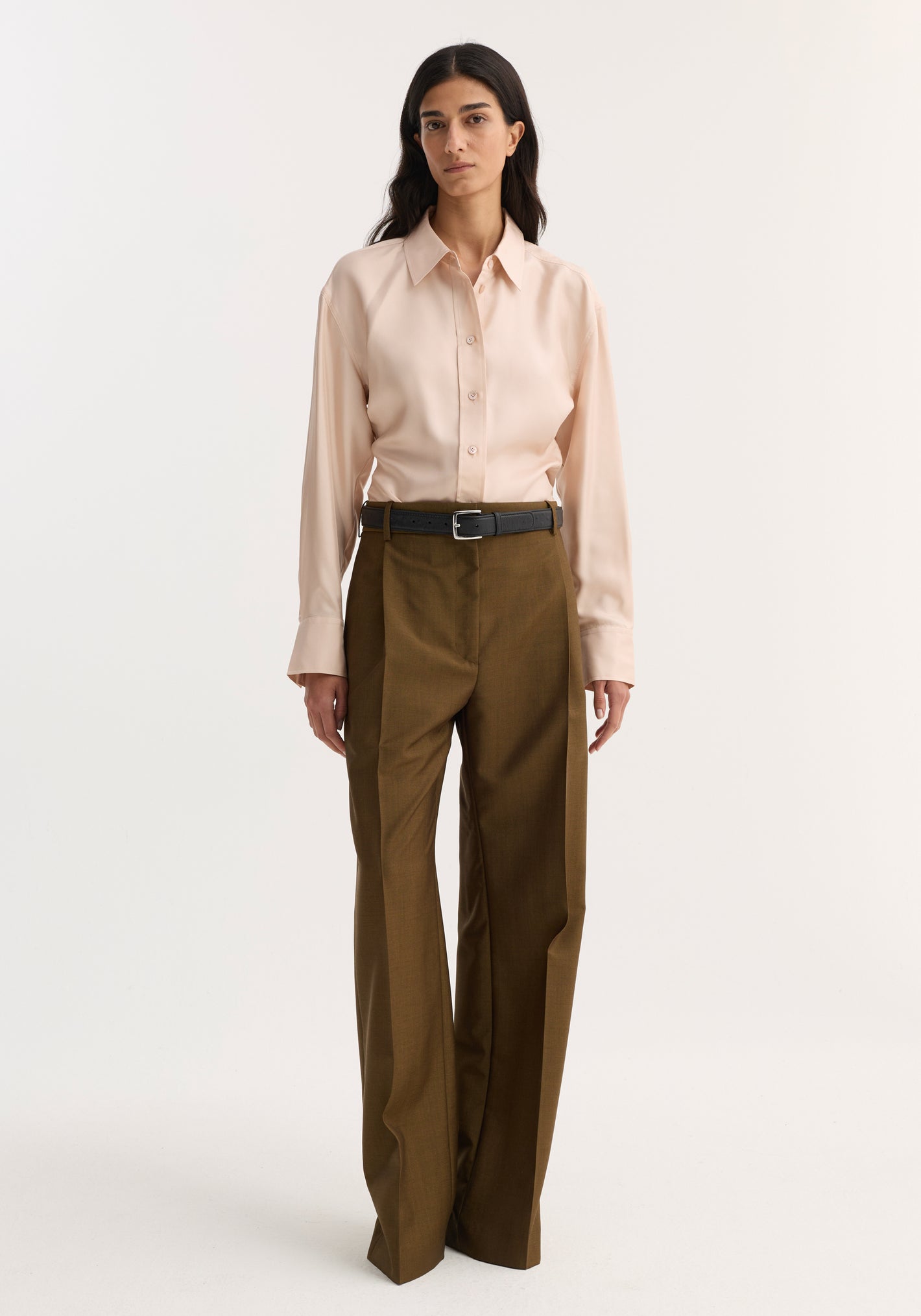 Woman wearing Relaxed straight leg trouser in golden brown, showcasing mid-rise fit with sharp front pleats and side pockets, paired with a tucked-in button-up shirt.