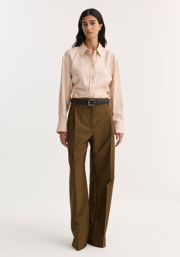 Woman wearing Relaxed straight leg trouser in golden brown, showcasing mid-rise fit with sharp front pleats and side pockets, paired with a tucked-in button-up shirt.