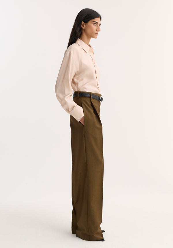 Model in profile wearing Relaxed straight leg trouser | golden brown, featuring sharp pleats, tailored waistband, and side pockets. Paired with a tucked-in blush-pink shirt.