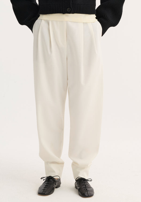 Barrel leg trousers in off-white, showcasing a loose fit with tapered ankles and double pleats, paired with black leather lace-up flats.