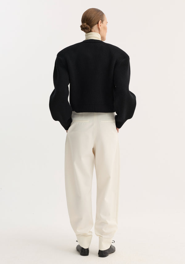 Back view of a model wearing Barrel leg trousers | off white, featuring a high-rise fit, wide curved legs, and ankle cuffs, paired with a black sweater.