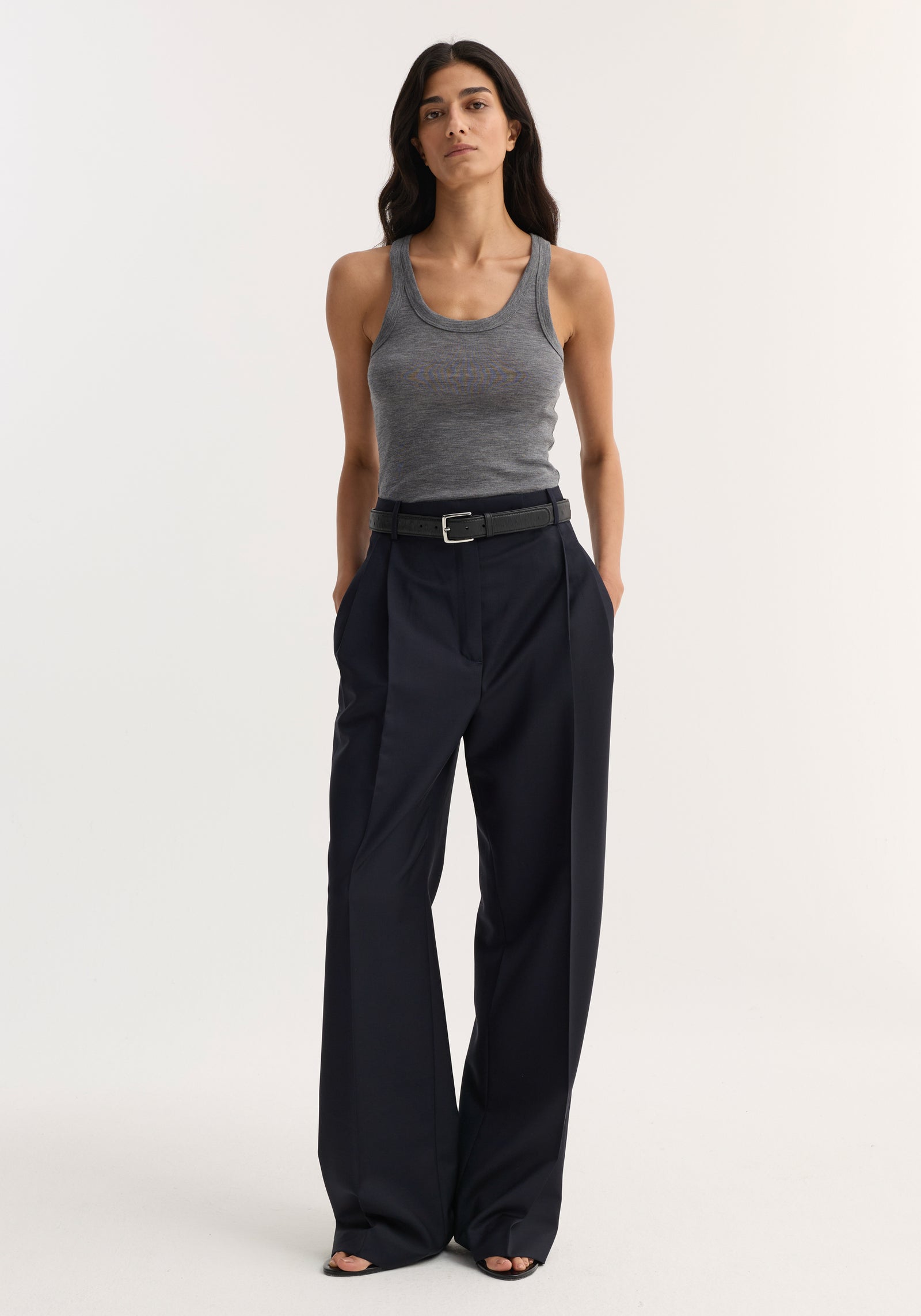 Person in heather-gray tank and Mid-waist tailored trousers, navy, with wide-leg cut and black belt. Hands in pockets, wearing black open-toe sandals.