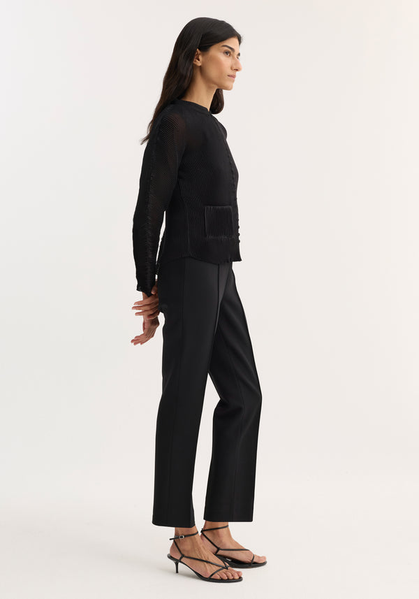 Woman in profile wearing fitted top and Cigarette leg trousers | black, showcasing pin-tuck detail and ankle-length design, hands clasped behind, looking right.