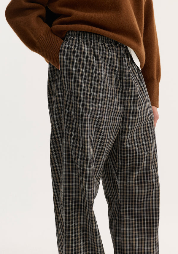 Model wearing Relaxed fit trousers in black/brown check, featuring a wide-leg design, elastic drawstring waistband, and side pockets, showcasing a comfortable, everyday style.