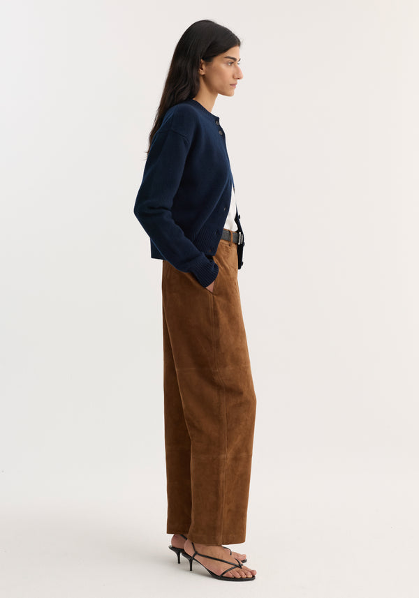 Woman in profile wearing Suede barrel leg trouser | tobacco, featuring wide legs, panel seam detailing, hands in pockets, paired with a navy cardigan and heeled sandals.