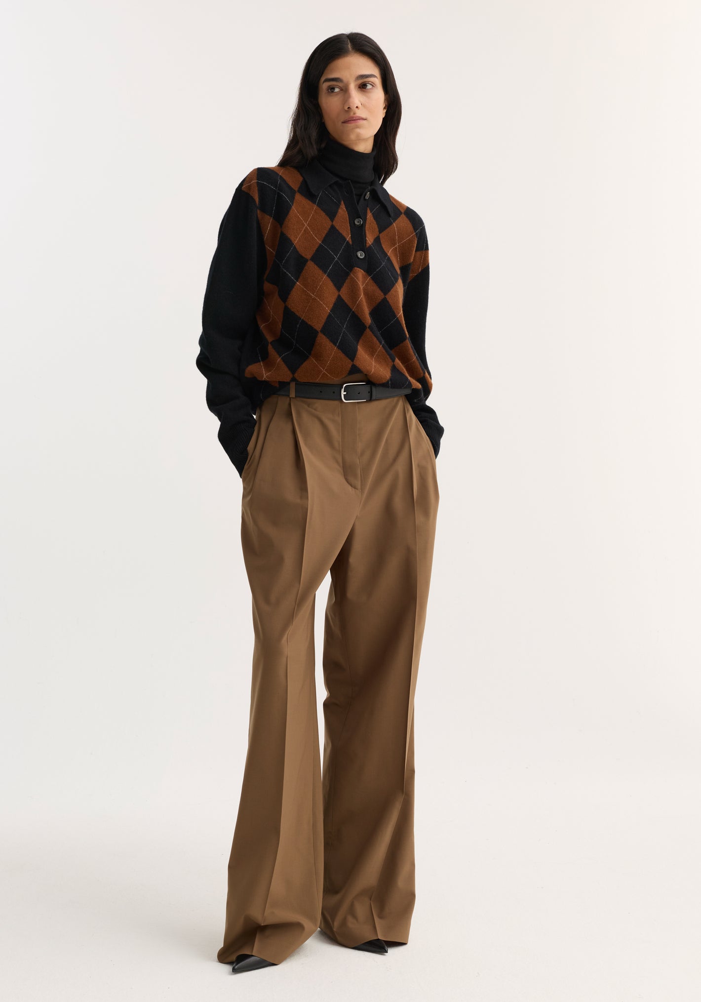 Model wearing Mid-waist tailored trousers in mocha with a structured waistband, double pleats, and wide legs, styled with a black and brown sweater.