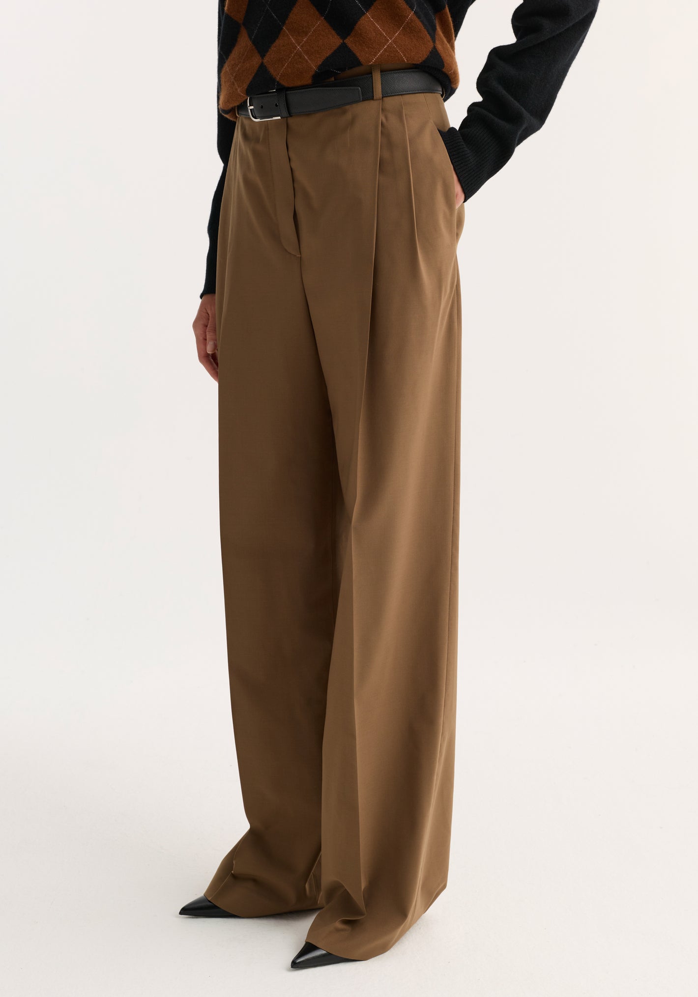 Model wearing mid-waist tailored trousers in mocha, featuring wide legs, a slim black belt, and pointed-toe shoes, against a white background.