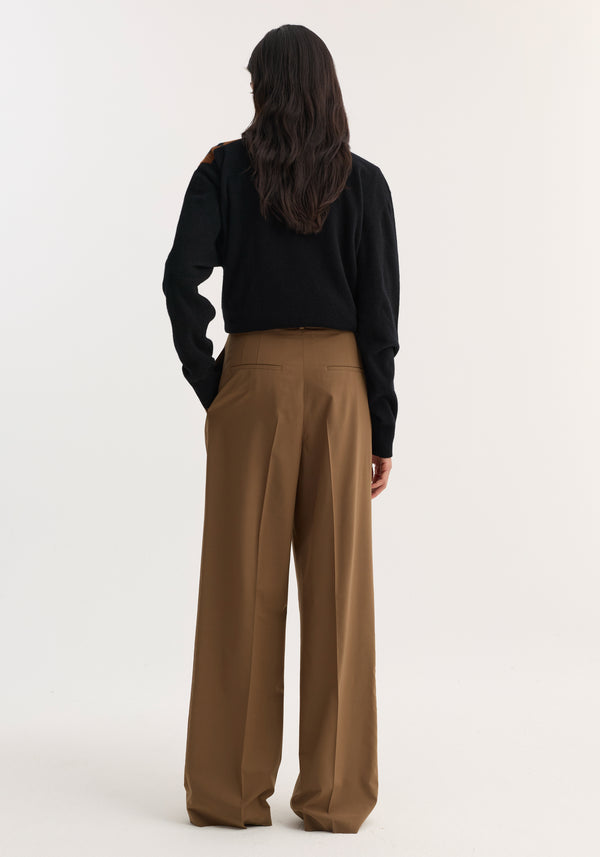 Person in black top, wearing Mid-waist tailored trousers | mocha, with wide legs, structured waistband, and double pleats, standing with hands in pockets.