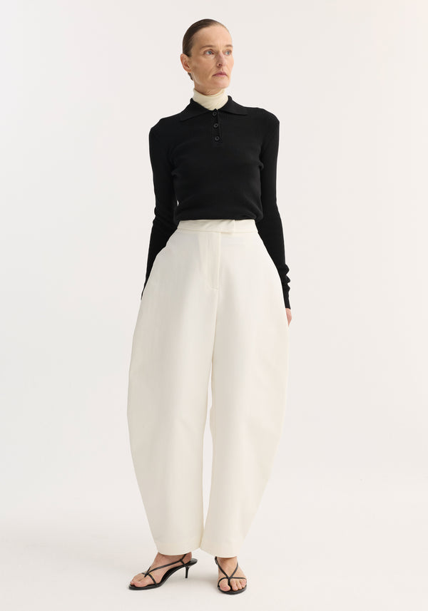 Model wearing sculptural trousers | paper white with a balloon leg and high waist, paired with a black polo-style top layered over a turtleneck.