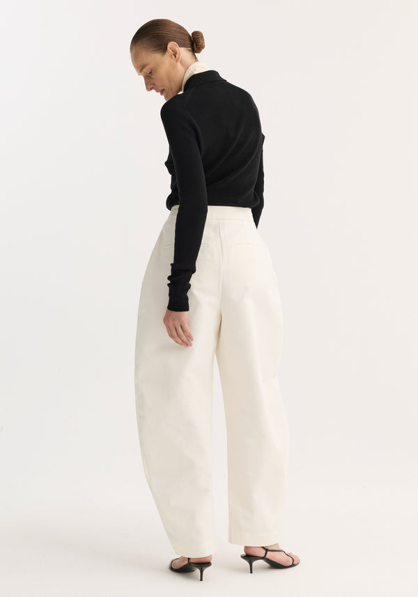Person in fitted black top and Sculptural trousers | paper white with balloon leg and high waist, highlighting the modern silhouette against a light background.