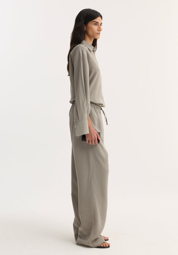 Woman in profile wearing Relaxed fit trousers | light grey stripe, featuring wide legs, drawstring waistband, and side seam pockets, paired with matching shirt.