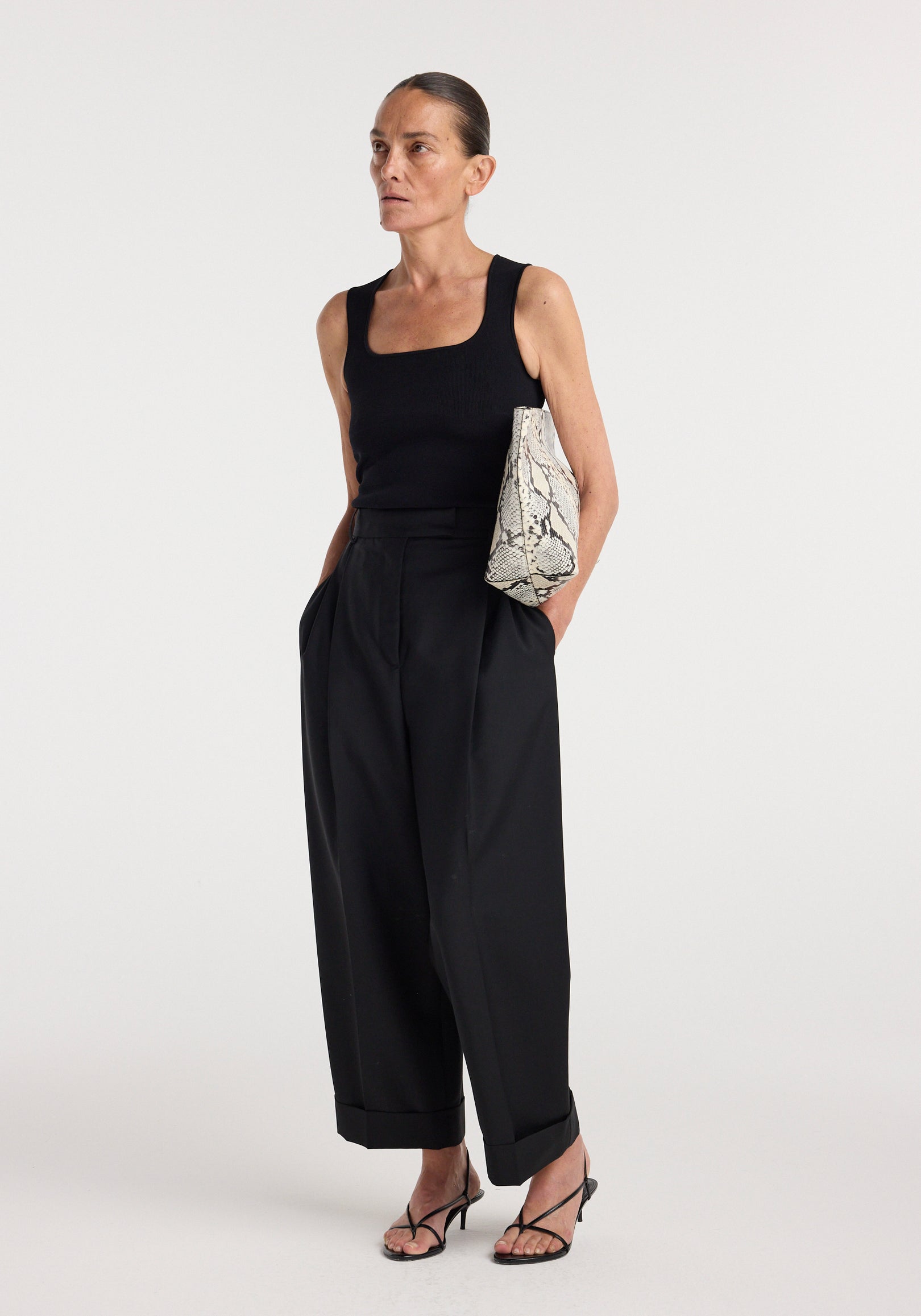 Woman wearing a black Bustier shaped knitted top | black paired with high-waisted wide-leg black pants, holding a snakeskin print clutch and wearing black strappy heels.