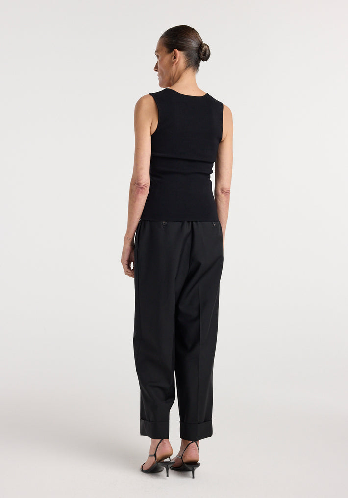 Woman seen from behind wearing a fitted sleeveless Bustier shaped knitted top | black paired with loose black trousers and strappy heeled sandals against a plain background.