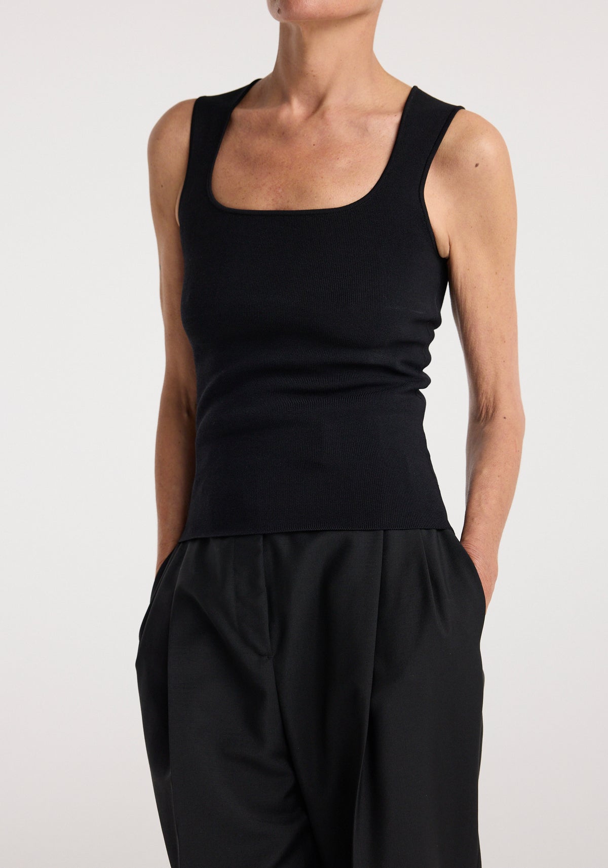 Woman wearing a sleeveless black fitted top with a square neckline paired with loose black pants, showcasing the Bustier shaped knitted top | black.