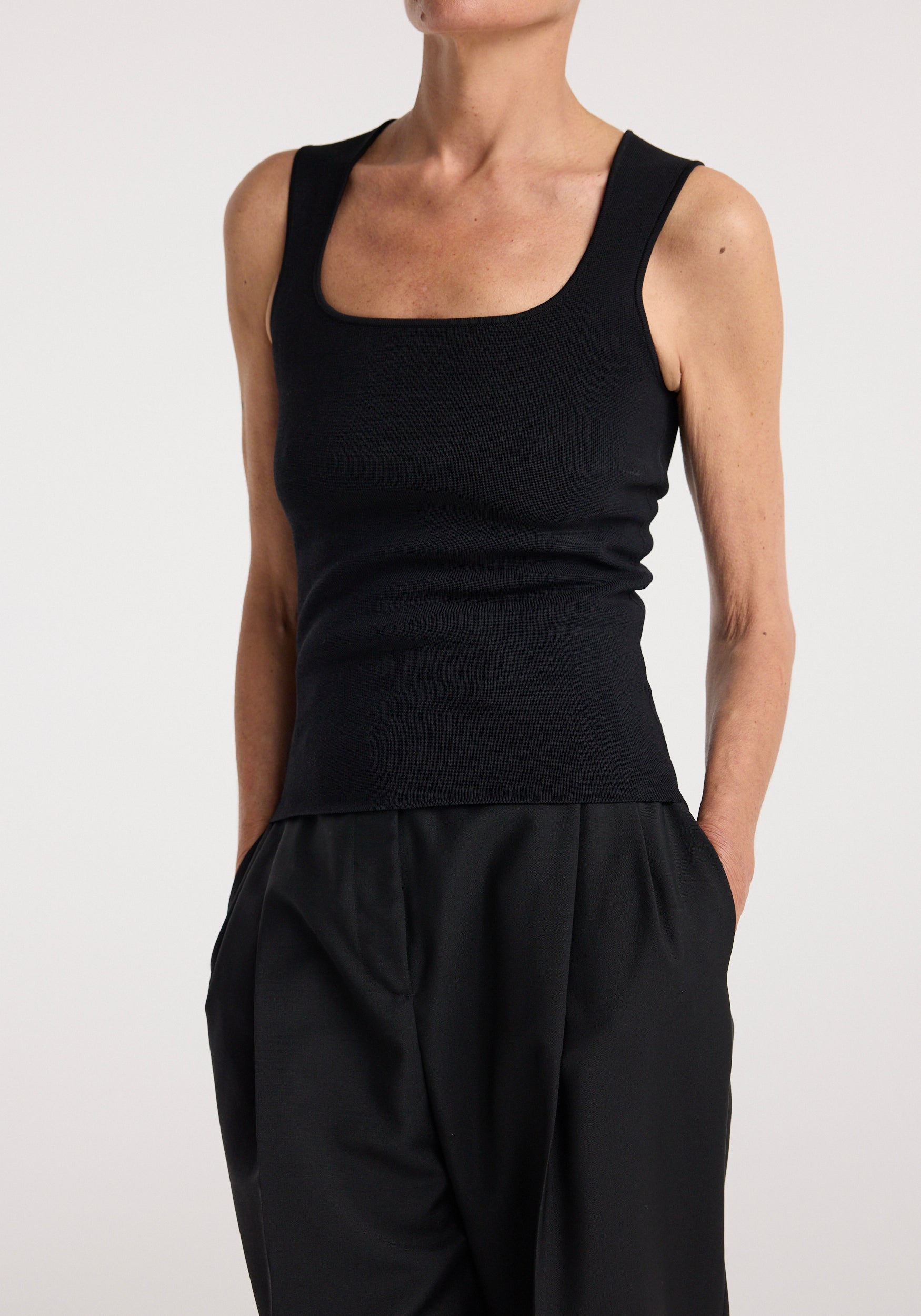 Woman wearing a sleeveless black fitted top with a square neckline paired with loose black pants, showcasing the Bustier shaped knitted top | black.