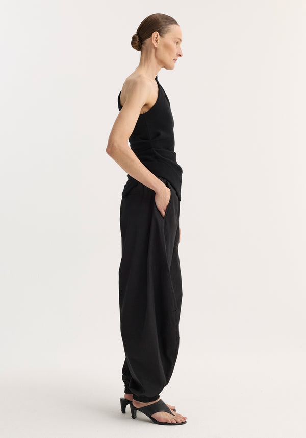 Model in Balloon track pants with elasticated waistband, crinkled texture, and welt pockets, paired with a one-shoulder top, showcasing a chic, modern silhouette.